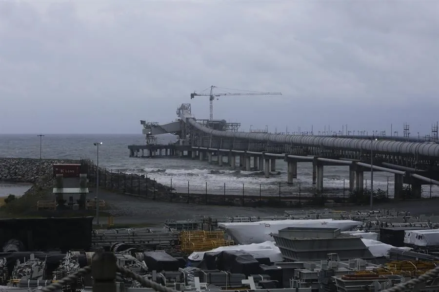 Infraestructura industrial con un largo muelle con tuberías que se extiende sobre el mar bajo un cielo nublado.