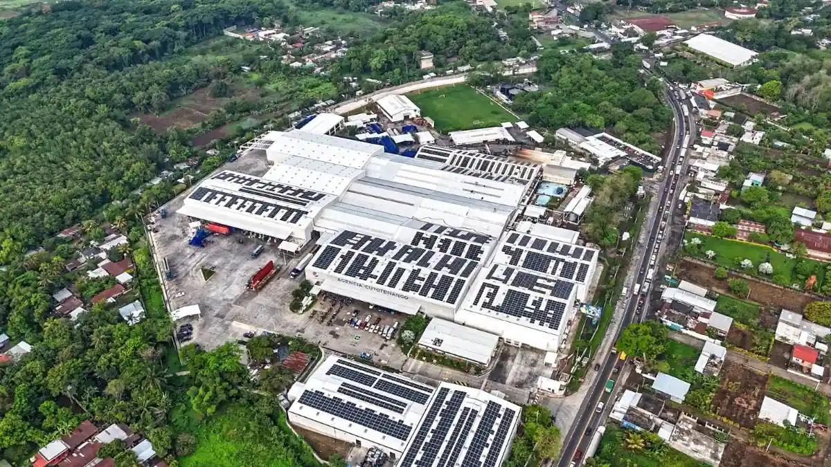 Vista aérea de una gran agencia empresarial con paneles solares instalados en el techo, rodeada de vegetación y una carretera con tráfico.