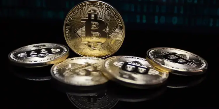 Moneda dorada de Bitcoin erguida rodeada de otras monedas sobre una superficie negra con reflejos y código binario.