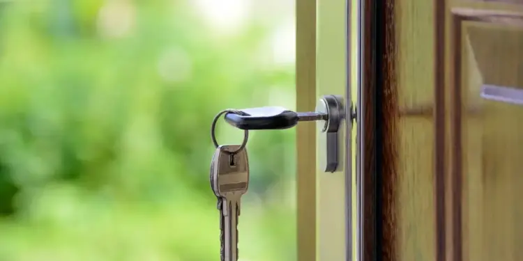 Llave metálica insertada en la cerradura de una puerta de madera entreabierta con fondo verde desenfocado.