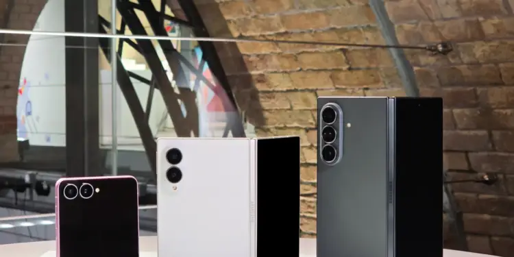 Tres teléfonos inteligentes plegables de diferentes colores sobre una mesa blanca frente a una pared de ladrillo.