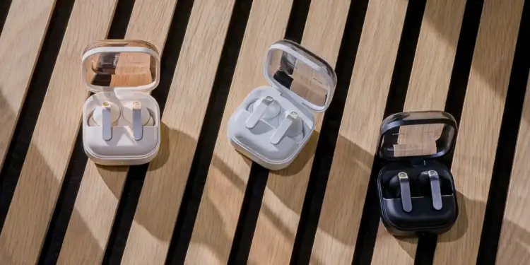 Tres estuches abiertos con auriculares inalámbricos en colores beige, blanco y negro sobre un fondo de listones de madera.