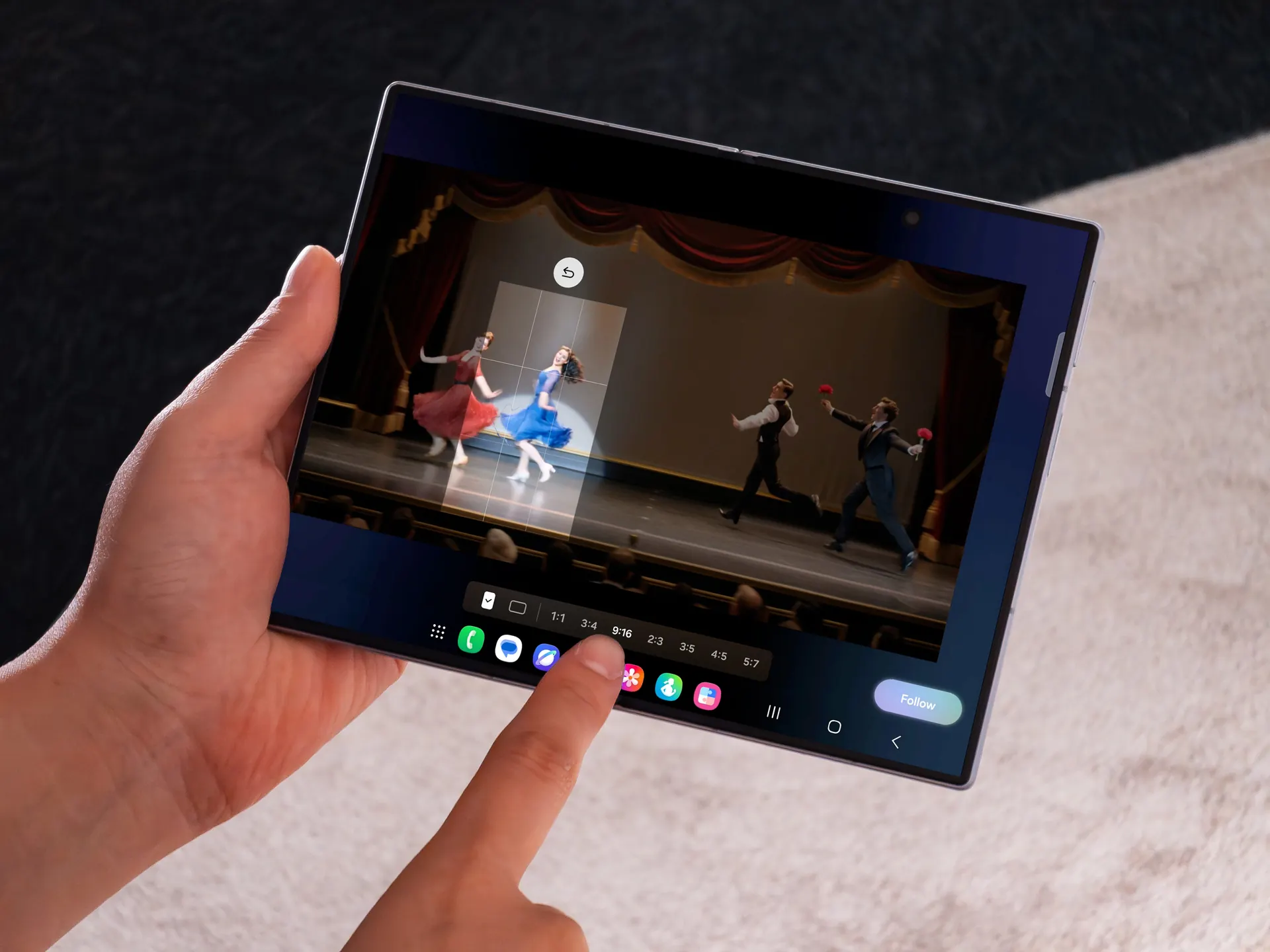 Manos sosteniendo una pantalla táctil plegable que muestra una interfaz de edición de video con bailarines en el escenario.