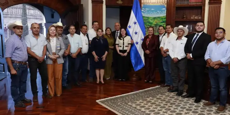 Grupo de hombres y mujeres de negocios y autoridades posando junto a la bandera de Honduras en una sala oficial.