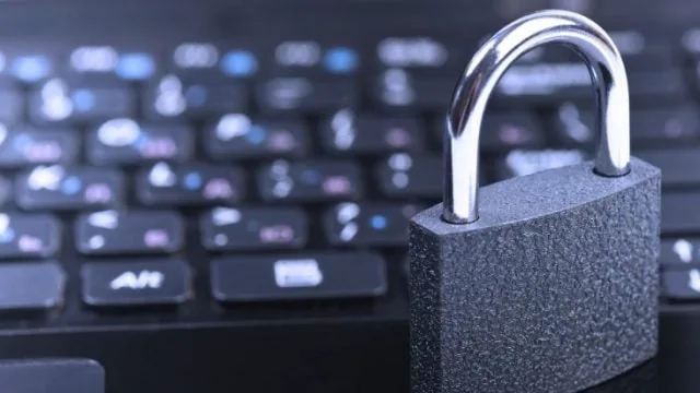 Candado metálico cerrado apoyado sobre el teclado negro de una computadora portátil.