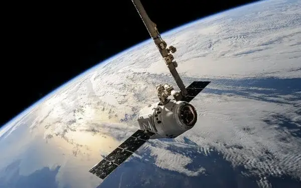 Nave espacial en órbita terrestre con paneles solares y la superficie de la Tierra de fondo.