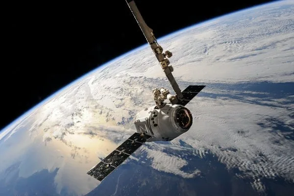 Nave espacial en órbita terrestre con paneles solares y la superficie de la Tierra de fondo.
