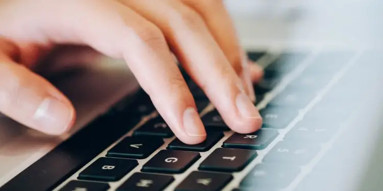 Mano de persona tecleando en un teclado de ordenador portátil. Se observan los dedos sobre las teclas oscuras con letras claras, enfocando la actividad digital.