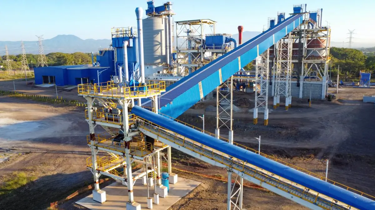 Vista aérea de una planta industrial moderna con estructuras metálicas azules y grandes cintas transportadoras.