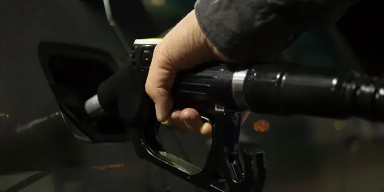 Mano de una persona sosteniendo una pistola surtidora de combustible para repostar un automóvil.