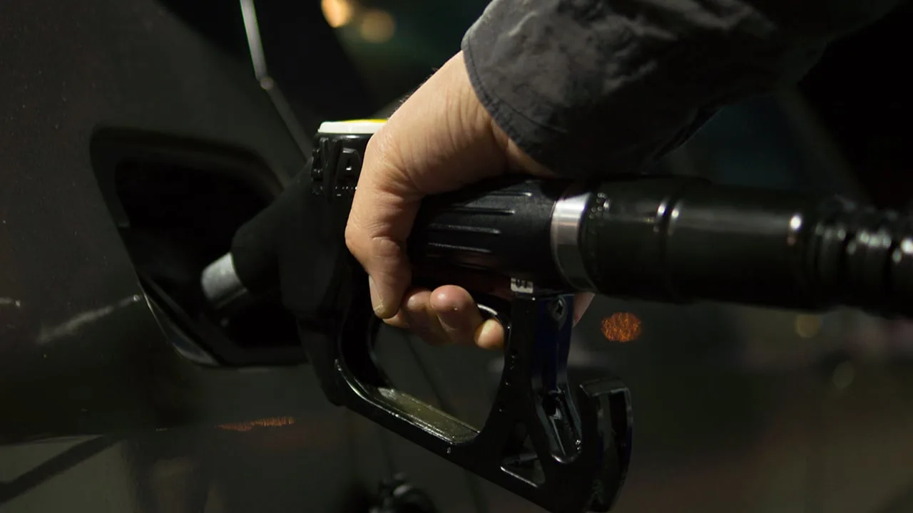 Mano de una persona sosteniendo una pistola surtidora de combustible para repostar un automóvil.