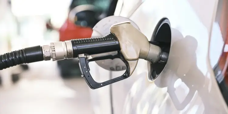 Boquilla de pistola dispensadora de combustible introducida en el tanque de un automóvil blanco en una gasolinera.
