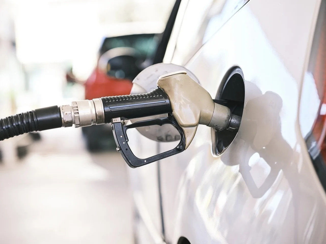 Boquilla de pistola dispensadora de combustible introducida en el tanque de un automóvil blanco en una gasolinera.