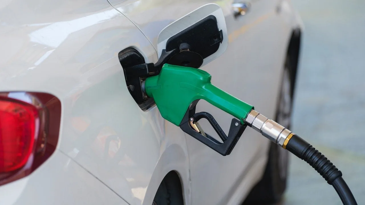 Primer plano de una manguera de combustible verde repostando gasolina en un coche blanco.