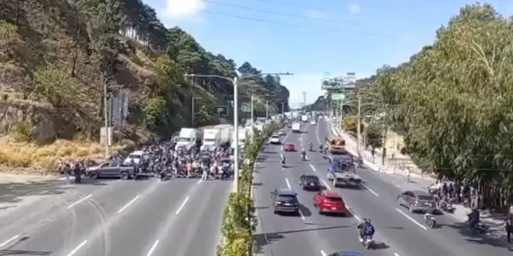 Vista aérea de una carretera dividida con tráfico fluido en un sentido y un bloqueo de manifestantes en el otro.