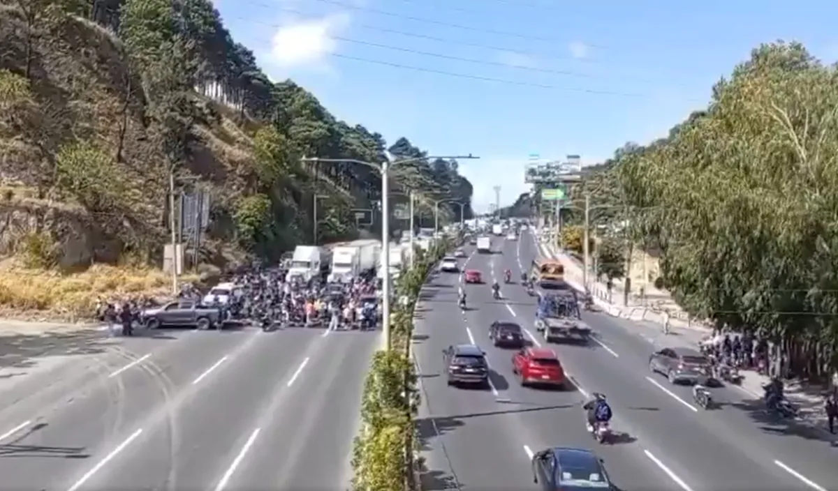 Vista aérea de una carretera dividida con tráfico fluido en un sentido y un bloqueo de manifestantes en el otro.