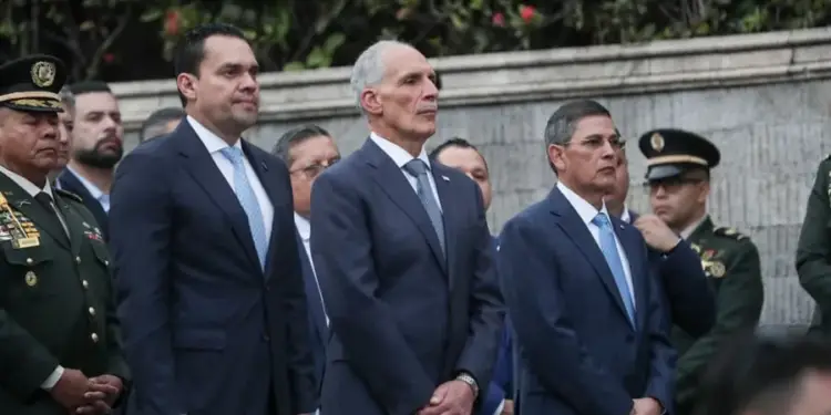 Grupo de hombres con traje formal y oficiales con uniforme militar asistiendo a un evento oficial y protocolario.
