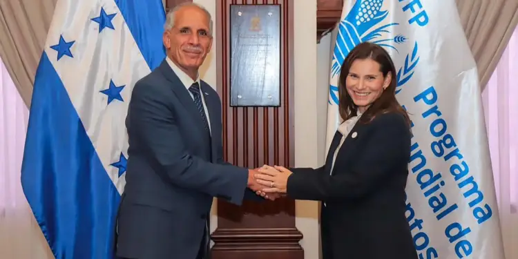 Hombre y mujer profesionales dándose la mano frente a las banderas de Honduras y el Programa Mundial de Alimentos, simbolizando un acuerdo.