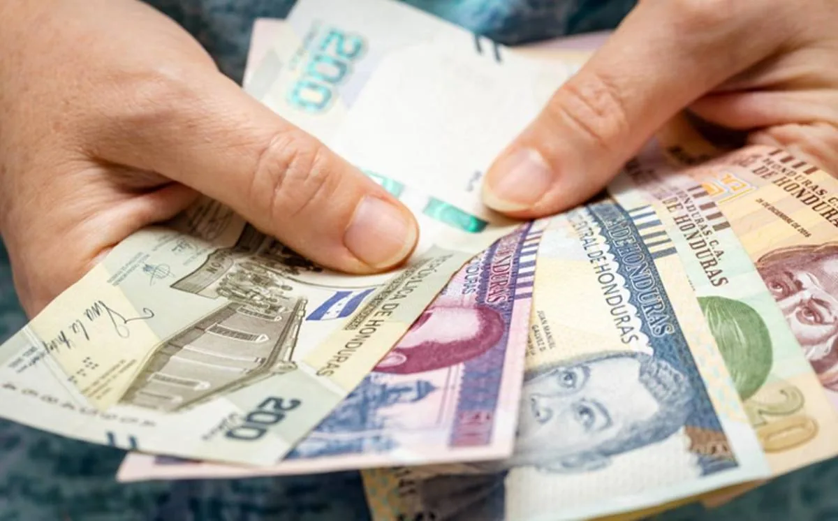 Manos sosteniendo y desplegando varios billetes en efectivo del Banco Central de Honduras de diferentes denominaciones.