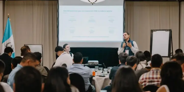 Orador presentando ante una audiencia en una conferencia empresarial con una pantalla de proyección al fondo