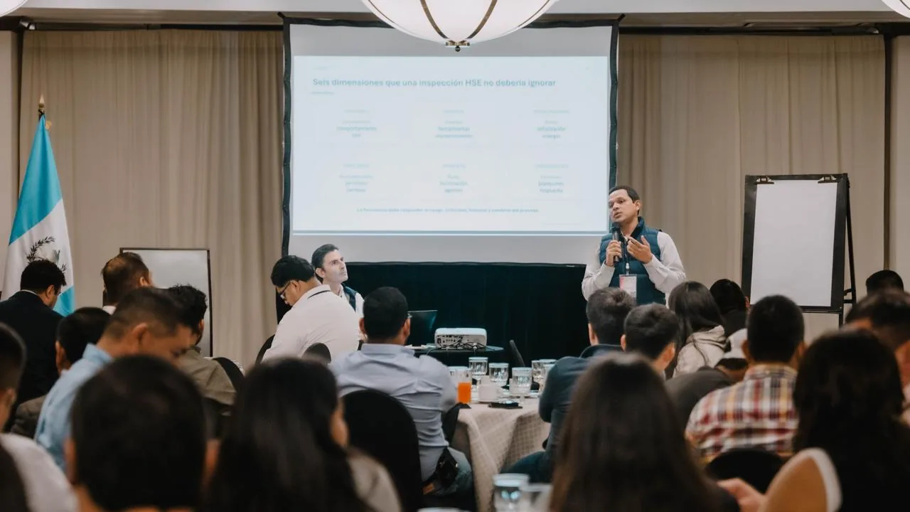 Orador presentando ante una audiencia en una conferencia empresarial con una pantalla de proyección al fondo