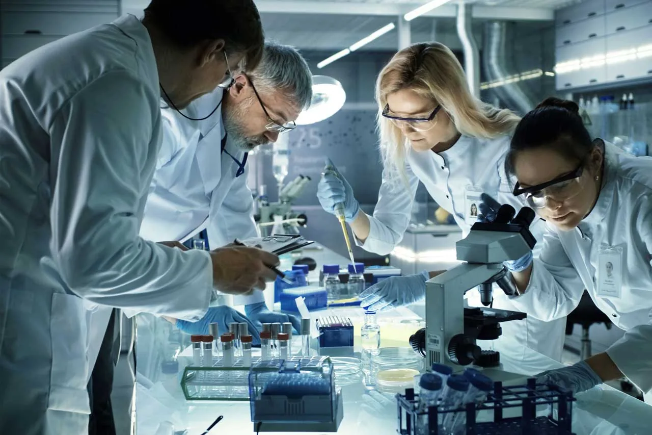 Equipo de científicos con batas blancas y gafas de seguridad trabajando juntos en un laboratorio moderno