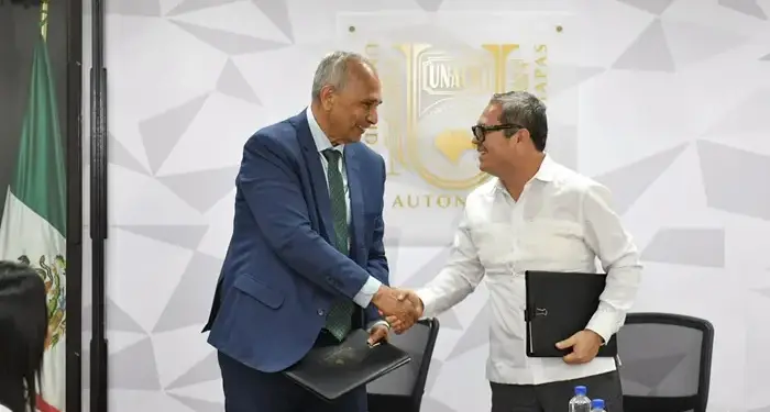 Dos hombres de negocios estrechando la mano tras firmar documentos en una oficina.