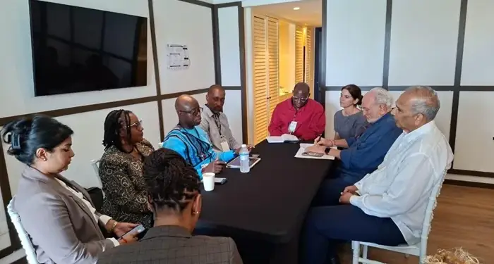 Un grupo diverso de profesionales reunidos alrededor de una mesa negra en una sala de juntas corporativa.