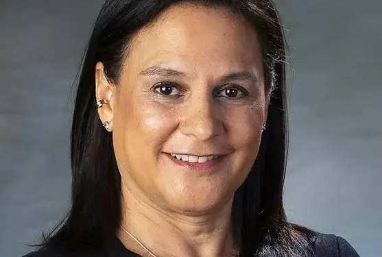 Retrato de media distancia de una mujer sonriente con cabello oscuro y blusa negra sobre fondo gris.