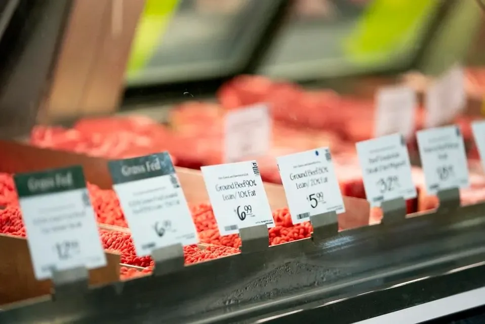 Vitrina refrigerada de supermercado con diversos cortes de carne fresca y etiquetas de precios visibles.