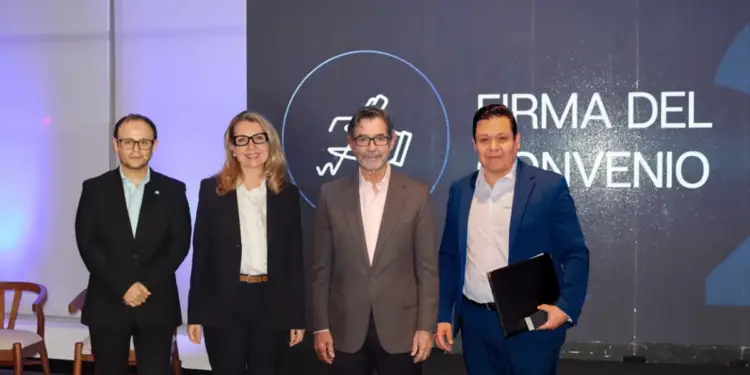 Cuatro profesionales de pie frente a una pantalla con el texto Firma del Convenio en un evento corporativo.