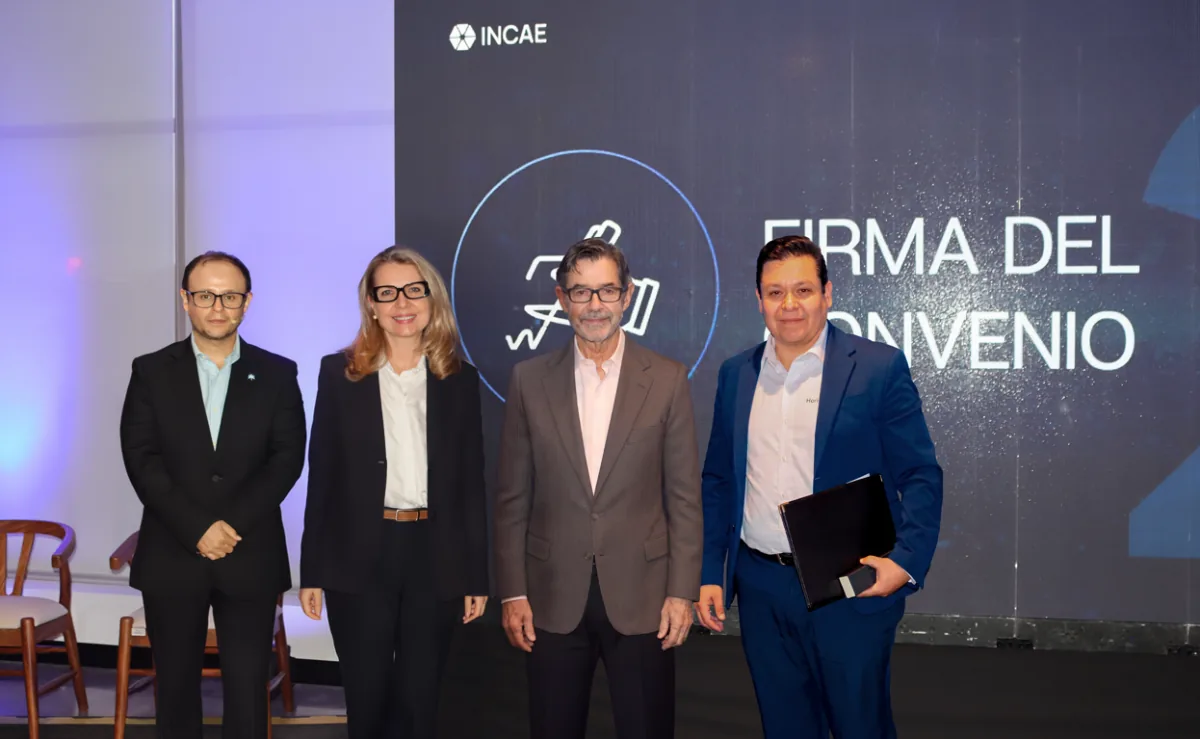 Cuatro profesionales de pie frente a una pantalla con el texto Firma del Convenio en un evento corporativo.
