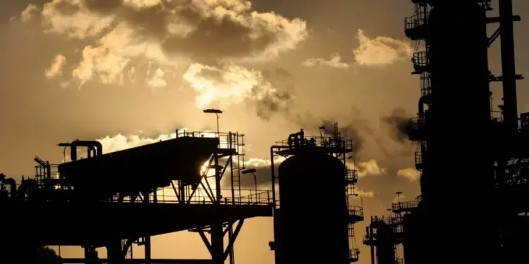 Silueta de una refinería o planta industrial con grandes torres y estructuras metálicas contra un cielo al atardecer.