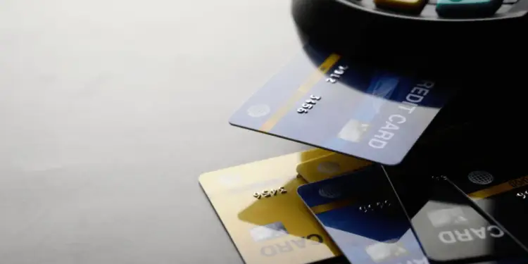 Varias tarjetas de crédito (azul, dorado, negro) con una insertada en un terminal de punto de venta (POS). Teclas visibles.