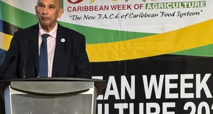 Hombre en traje hablando en podio durante la Semana de Agricultura del Caribe 2026 en Jamaica, con logo del Ministerio de Agricultura.