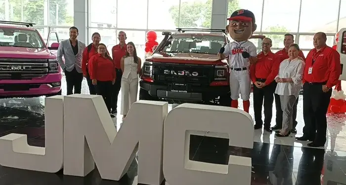 Grupo de personas posando junto a camionetas y letras corpóreas gigantes en un concesionario de vehículos.