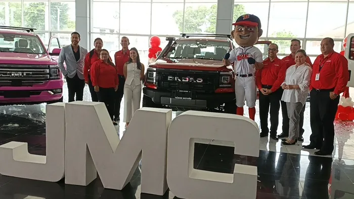 Grupo de personas posando junto a camionetas y letras corpóreas gigantes en un concesionario de vehículos.