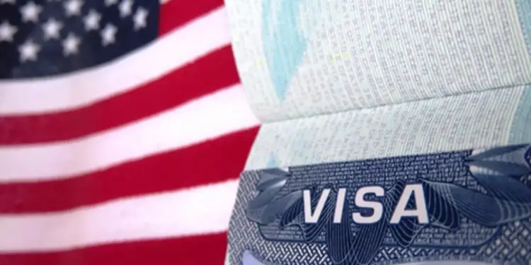 Primer plano de un pasaporte abierto mostrando una visa frente a la bandera de Estados Unidos.