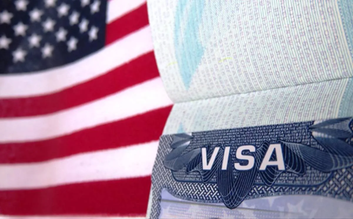 Primer plano de un pasaporte abierto mostrando una visa frente a la bandera de Estados Unidos.