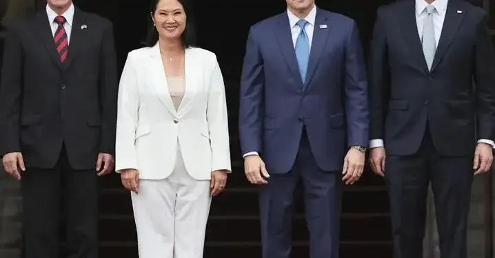Cuatro profesionales de pie vestidos con trajes formales en una entrada con alfombra roja.