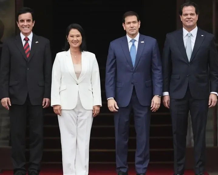Cuatro profesionales de pie vestidos con trajes formales en una entrada con alfombra roja.