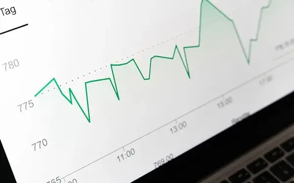 Gráfico de líneas verdes que muestra la fluctuación de valores financieros en la pantalla de una laptop.