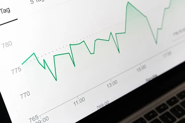 Gráfico de líneas verdes que muestra la fluctuación de valores financieros en la pantalla de una laptop.