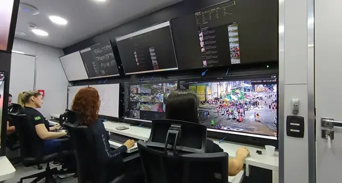 Tres profesionales trabajando frente a un panel con múltiples pantallas de monitoreo en una oficina moderna.