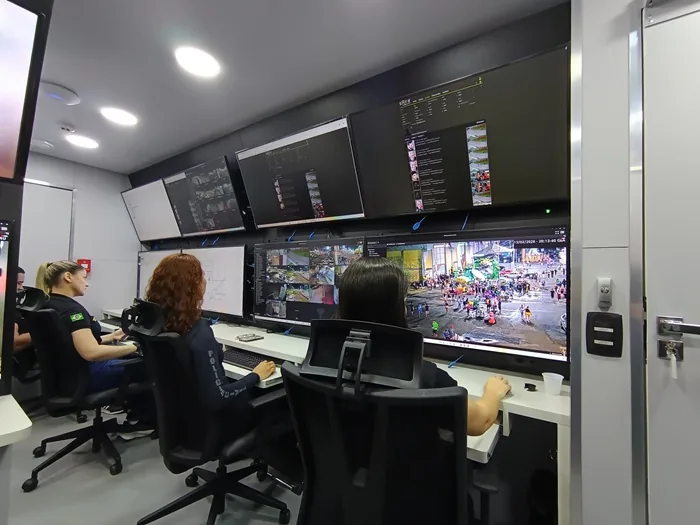 Tres profesionales trabajando frente a un panel con múltiples pantallas de monitoreo en una oficina moderna.