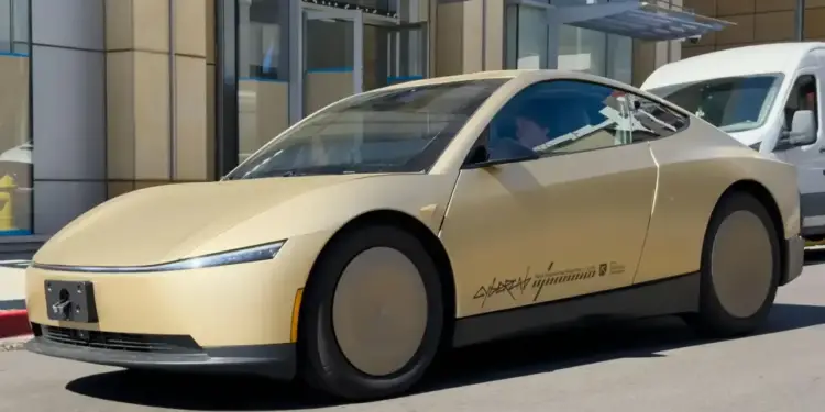 Vehículo cupé de color dorado futurista con ruedas tapadas estacionado frente a un edificio comercial moderno.