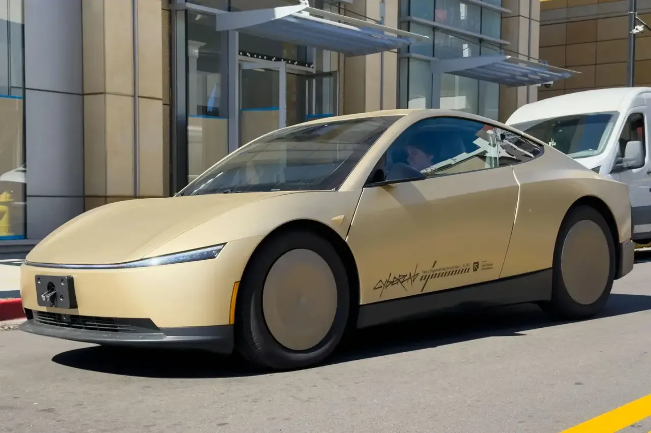 Vehículo cupé de color dorado futurista con ruedas tapadas estacionado frente a un edificio comercial moderno.