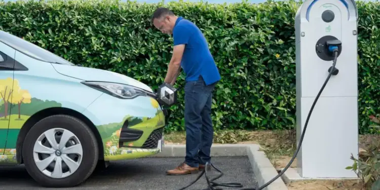 Hombre conectando un coche eléctrico a una estación de carga pública en el exterior.