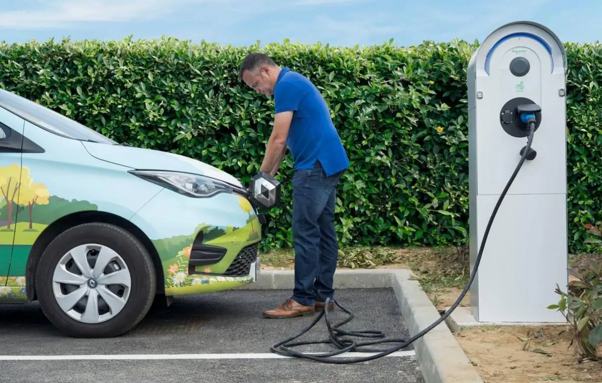 Hombre conectando un coche eléctrico a una estación de carga pública en el exterior.