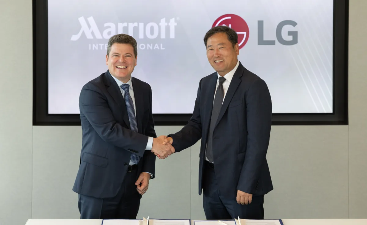 Dos ejecutivos estrechándose la mano frente a una pantalla con los logos de Marriott International y LG.